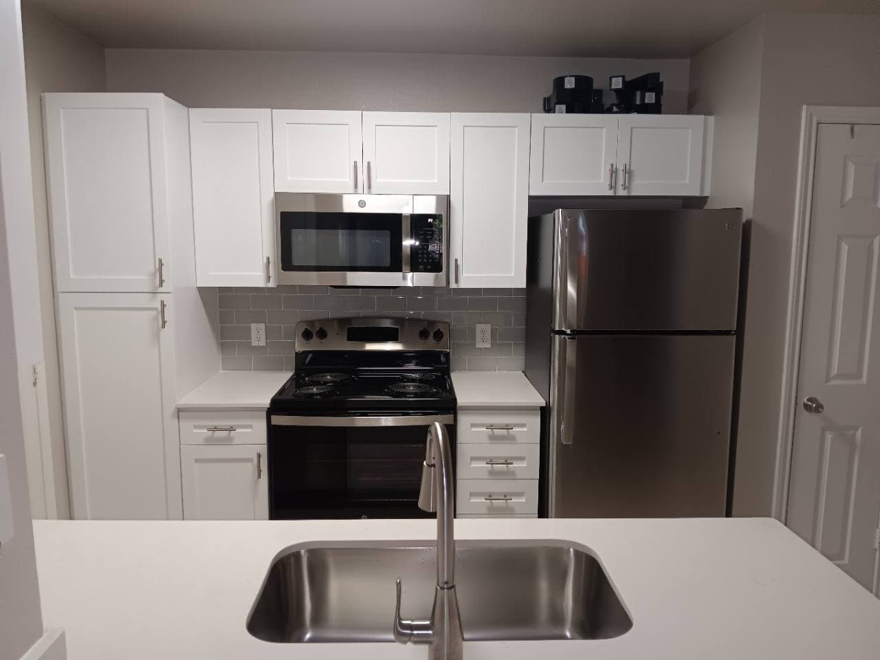 Finished apartment kitchen with white shaker cabinets, updated counters, and stainless appliances.