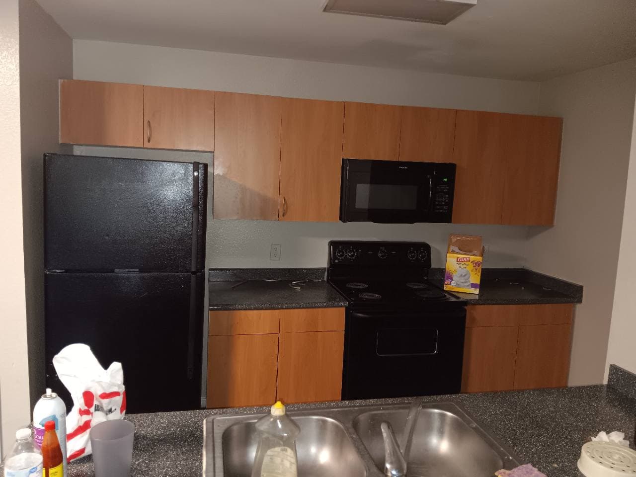 Older apartment kitchen with darker cabinets and black appliances before renovation.